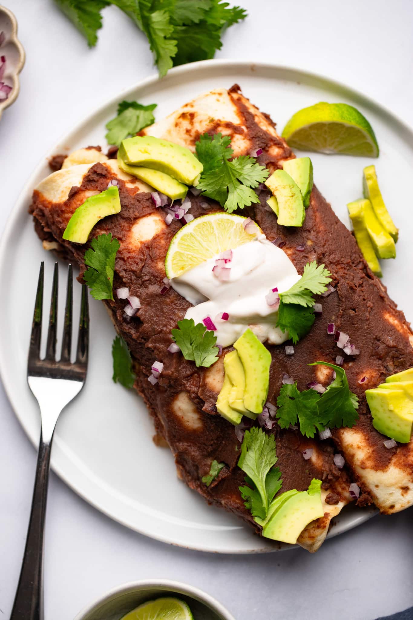 two Roasted Veggie Enchiladas with Black Bean Sauce on a white plate with a fork on the side.