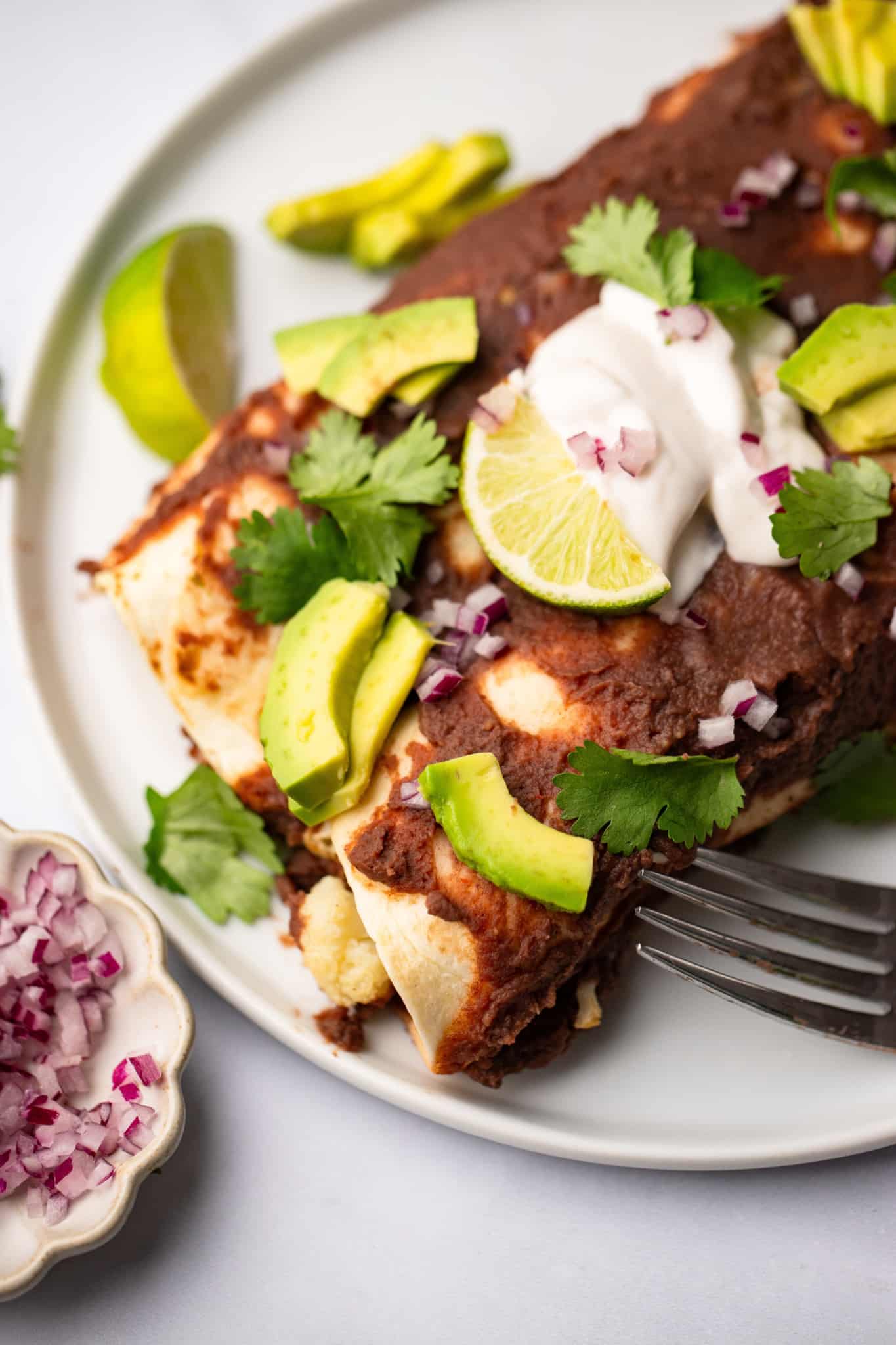 close up on Roasted Veggie Enchiladas with Black Bean Sauce on a white plate with a fork on the side.