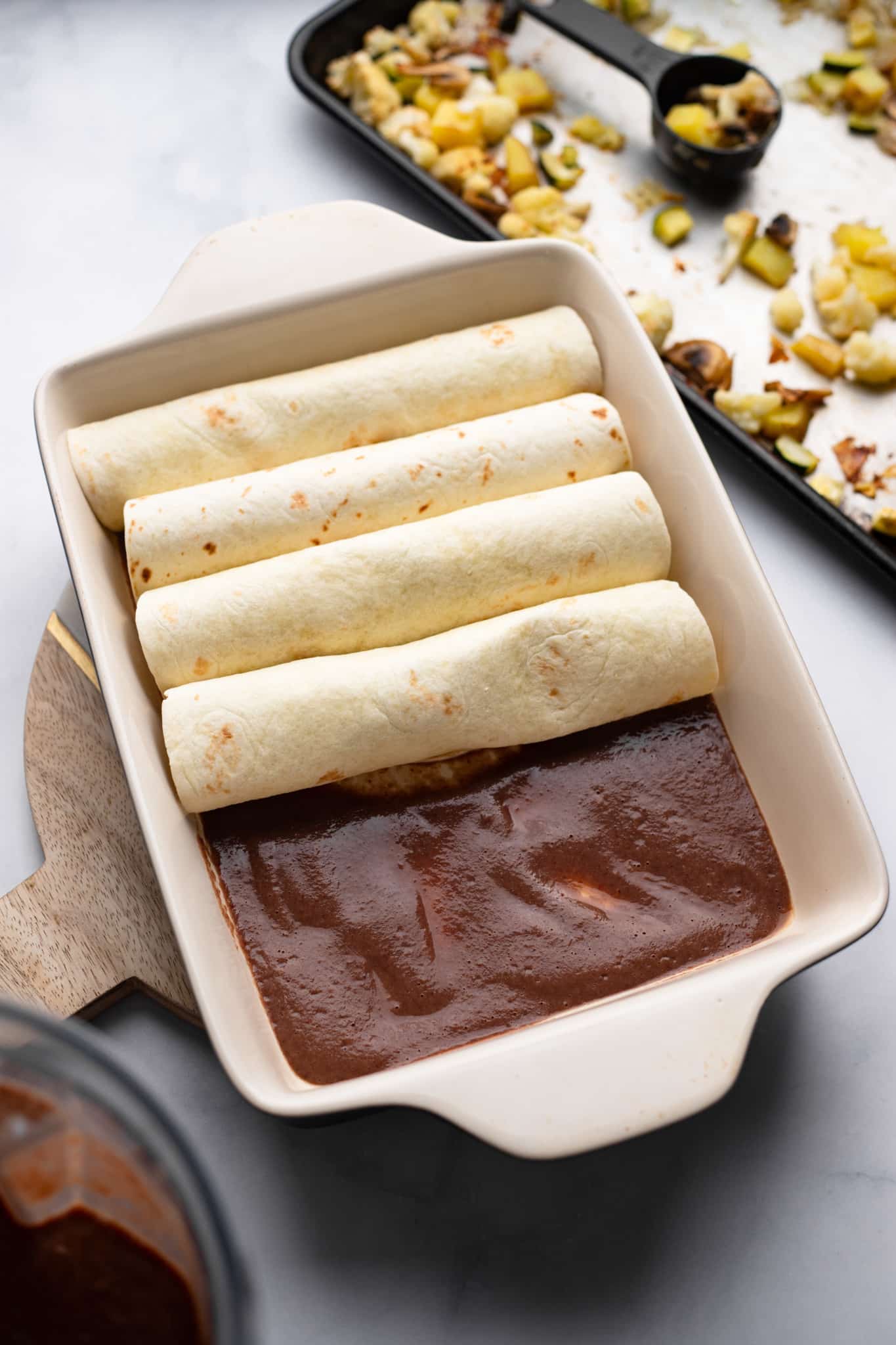 assembling Roasted Veggie Enchiladas with Black Bean Sauce in a baking dish.