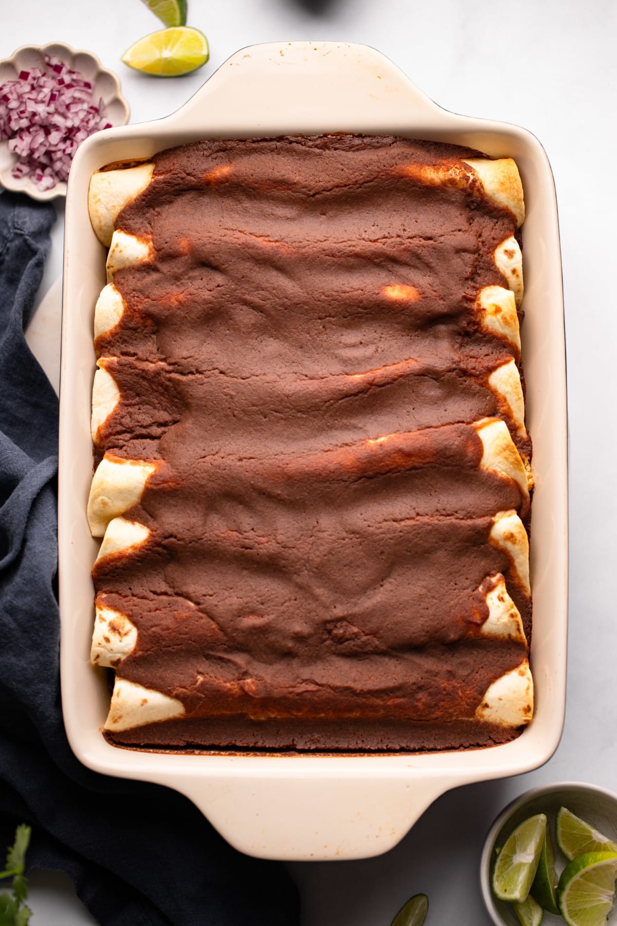 baked veggie enchiladas covered in black bean sauce in a baking dish.