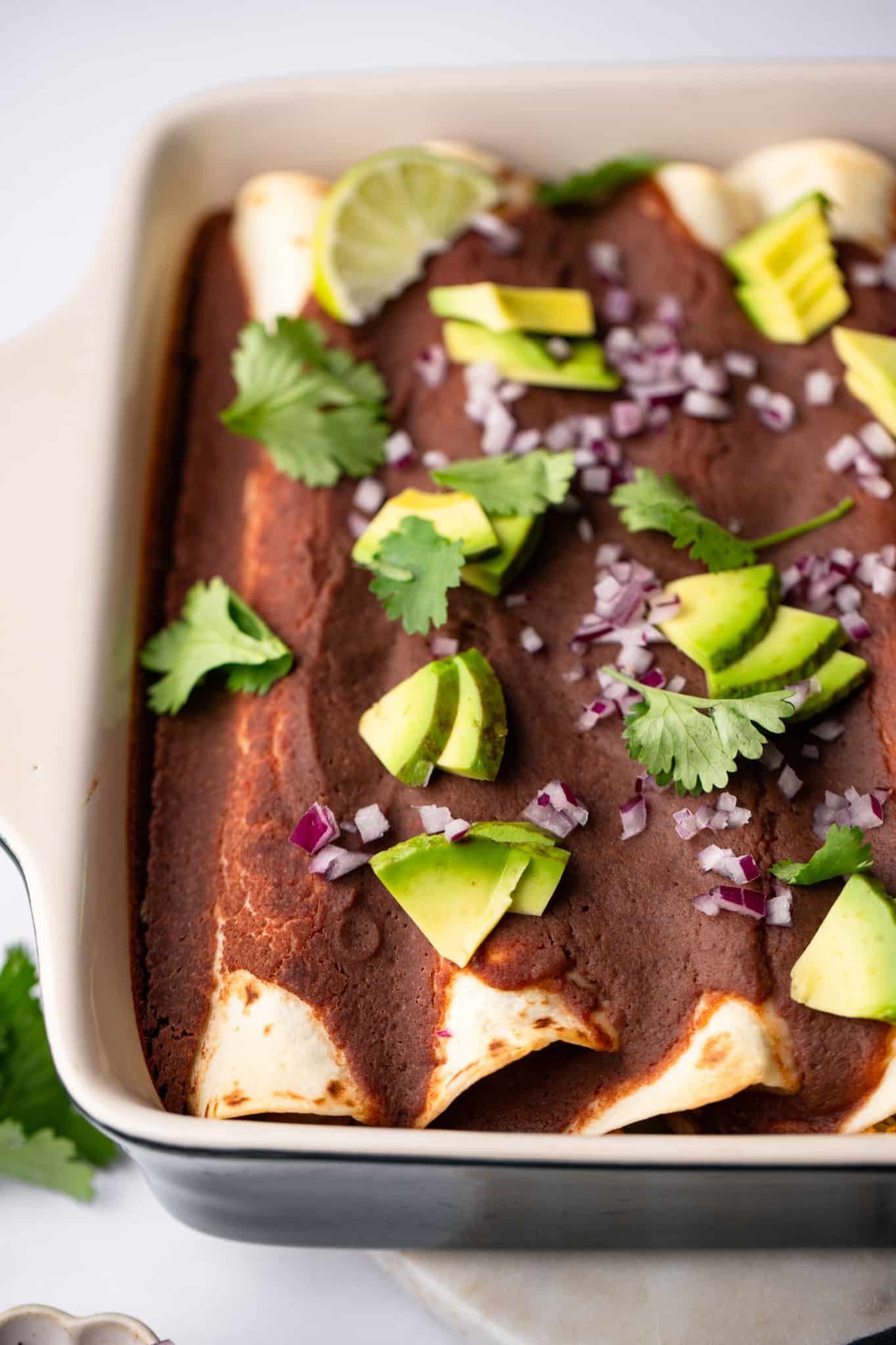 Roasted Veggie Enchiladas with Black Bean Sauce topped with avocado, onions, and cilantro in a baking dish.