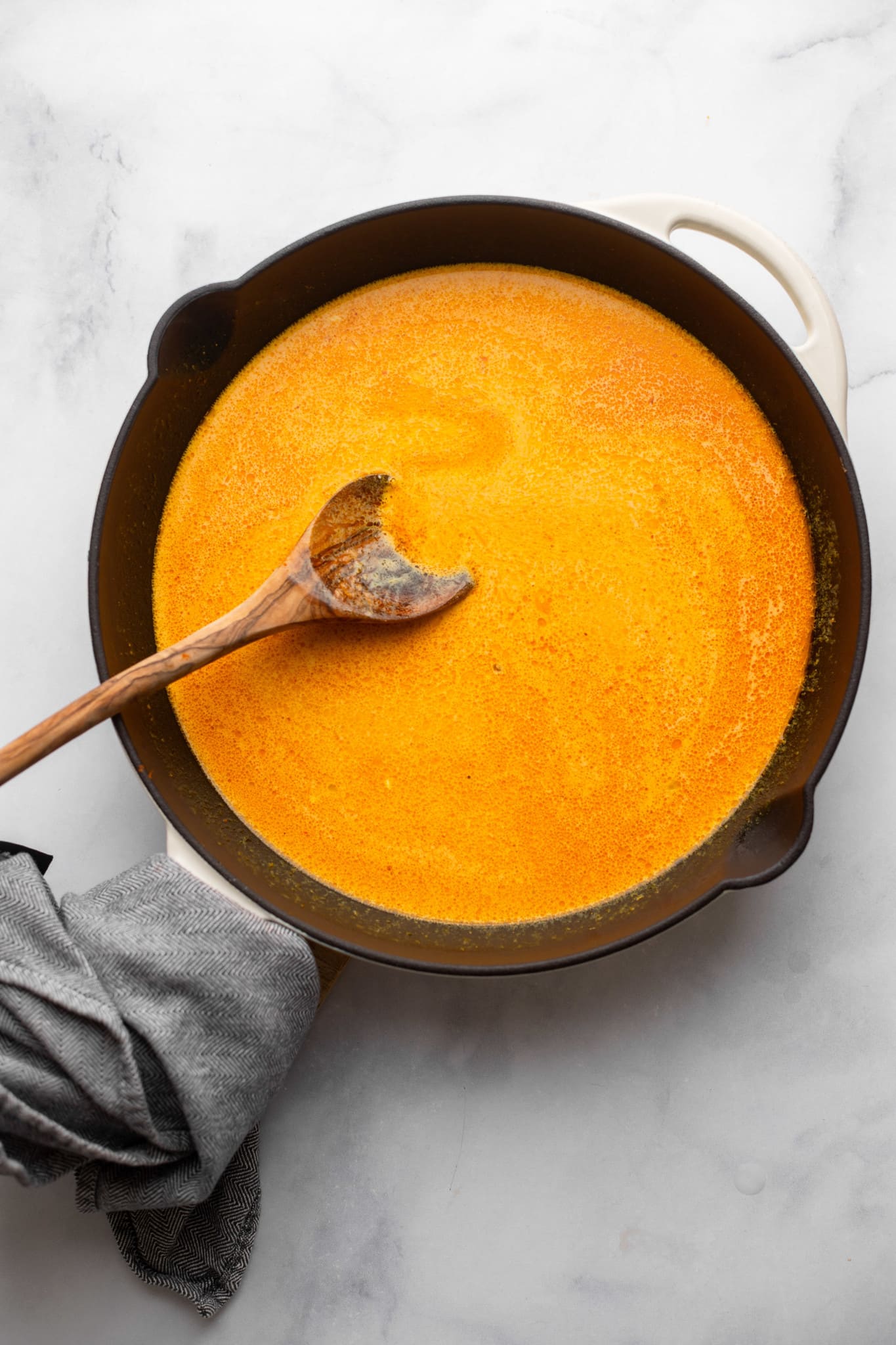 stirring red curry sauce with a wooden spoon in a black skillet.