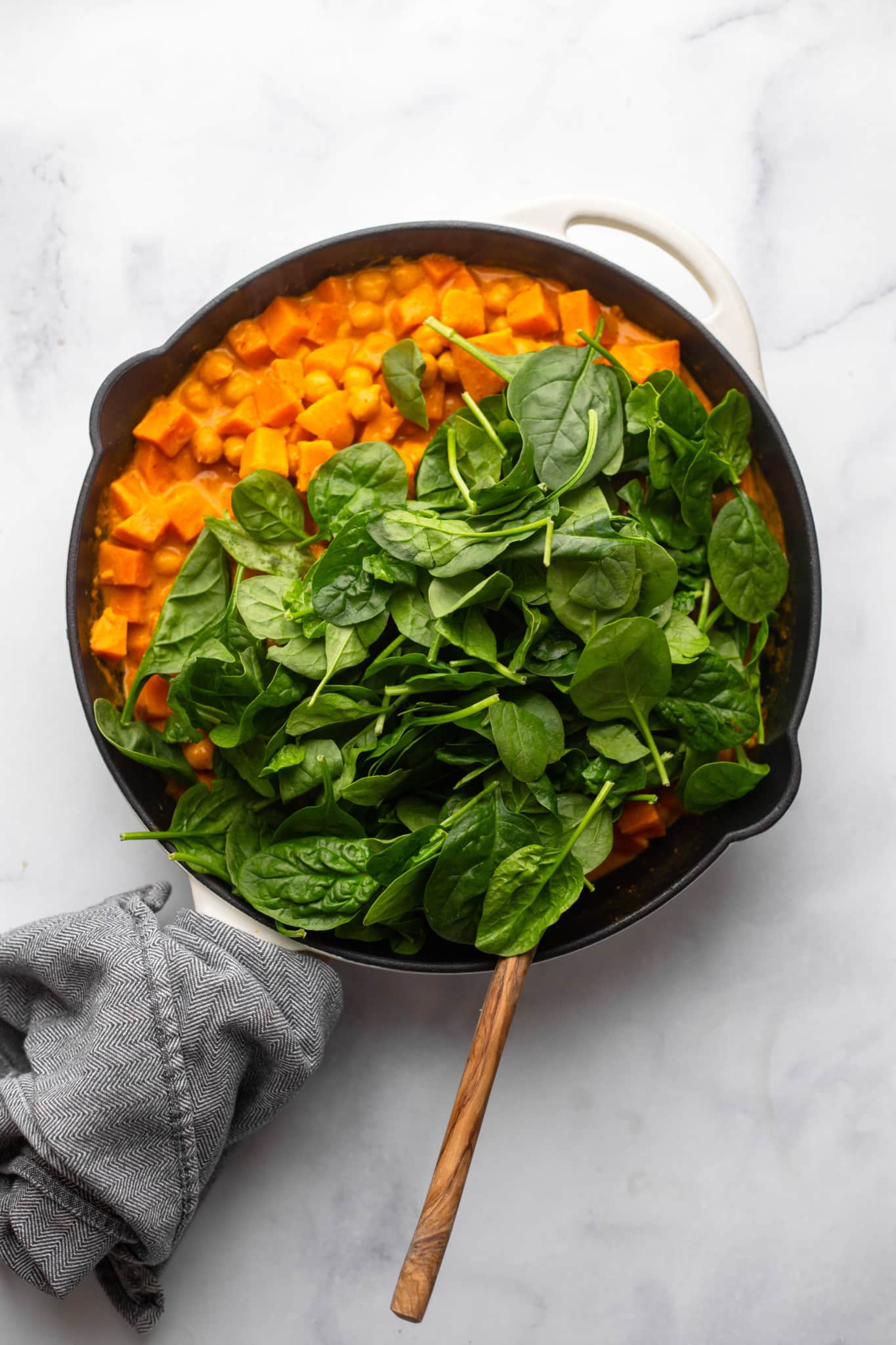 fresh spinach on top of red curry in a black skillet.