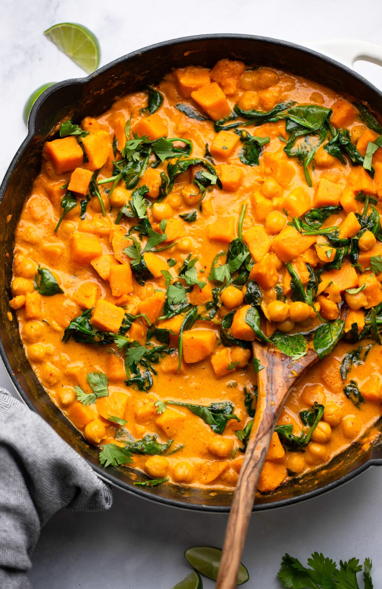 using a wooden spoon to scoop sweet potato curry in a black skillet.