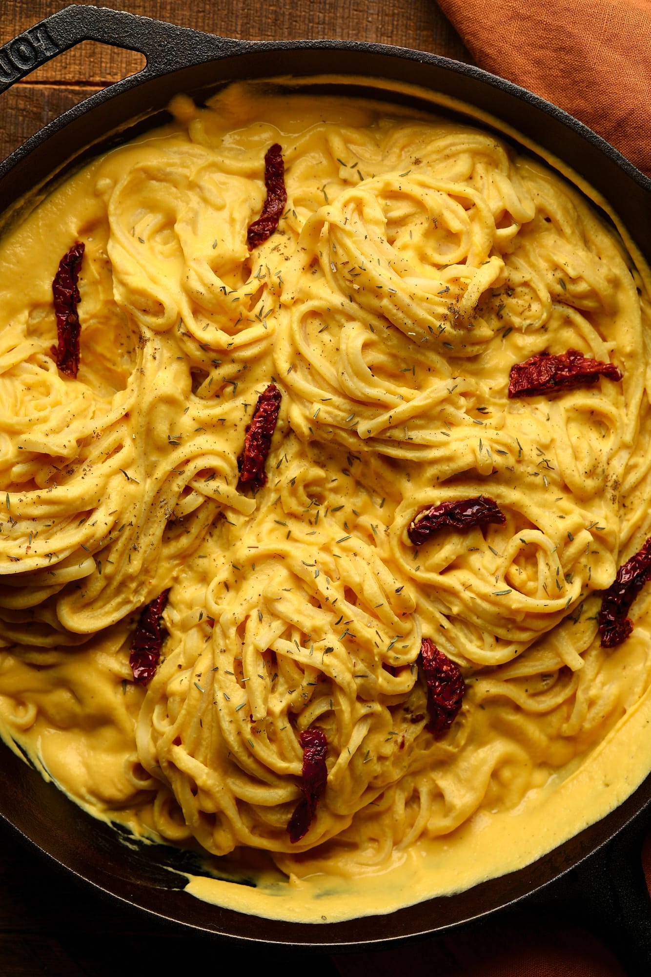 pan with yellow cream pasta and sun dried tomatoes, orange towel in wooden background