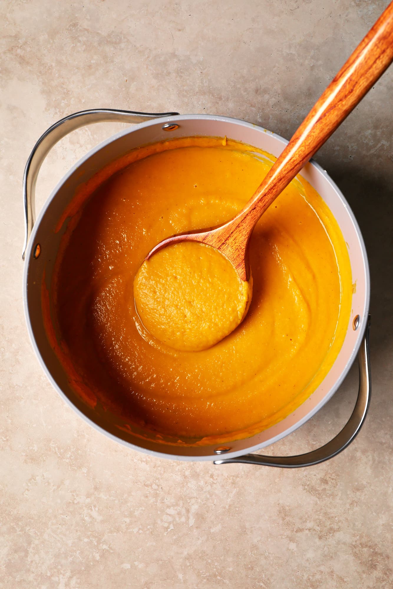 a wooden spoon in a pot of butternut squash and sweet potato soup.