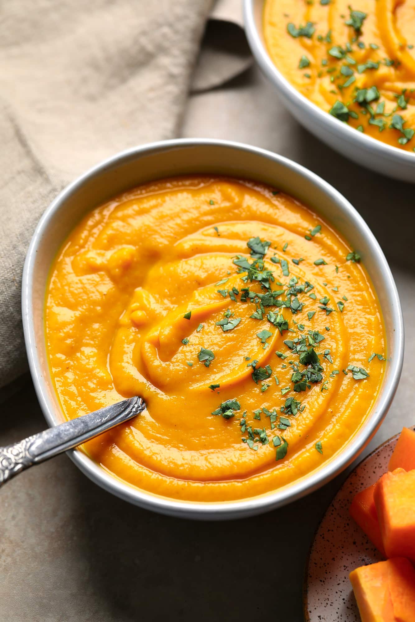 a bowl of Butternut Squash and Sweet Potato Soup topped with chopped herbs.