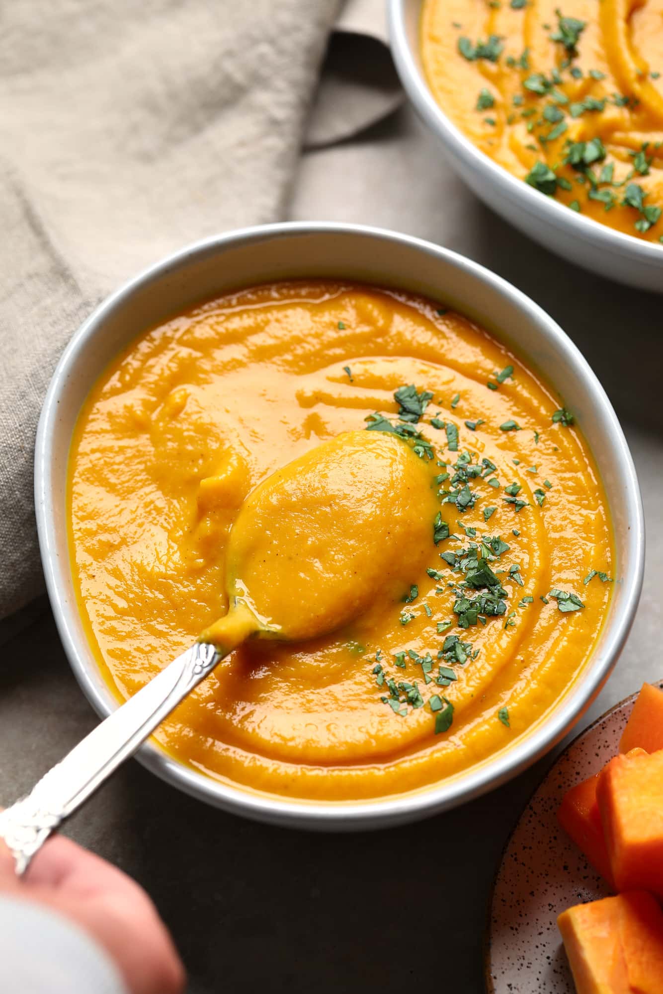 a hand lifting a spoon out of a bowl of Butternut Squash and Sweet Potato Soup.