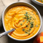 a bowl of Butternut Squash and Sweet Potato Soup topped with chopped herbs.