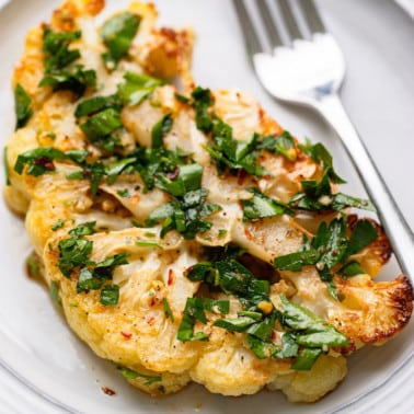 square image of a slice of roasted cauliflower with green stuff on top on a plate