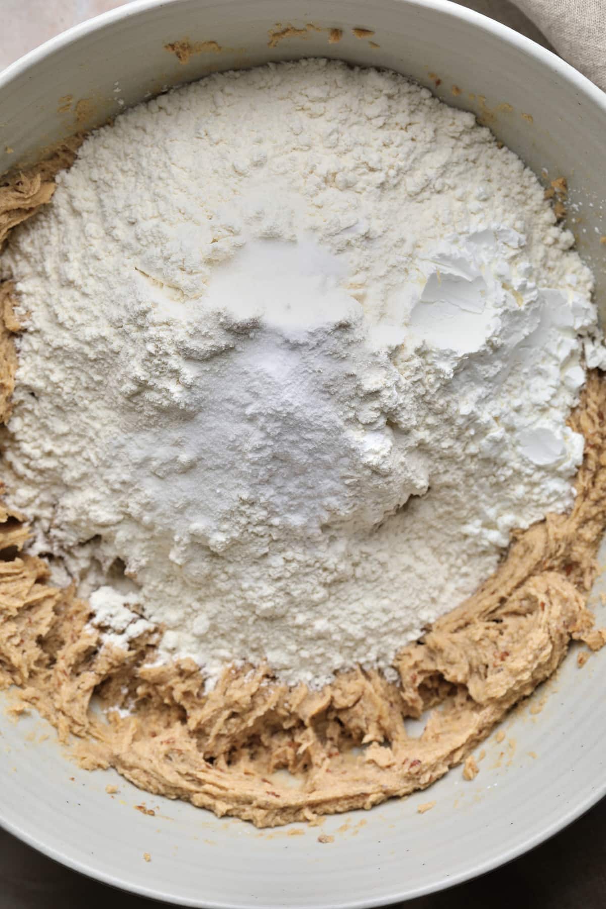 flour and other dry ingredients being added to beige mixture in bowl