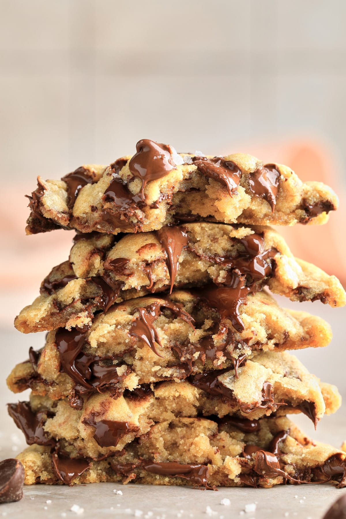 stack of several vegan chocolate chip cookies broken in half, grey background and pink towel