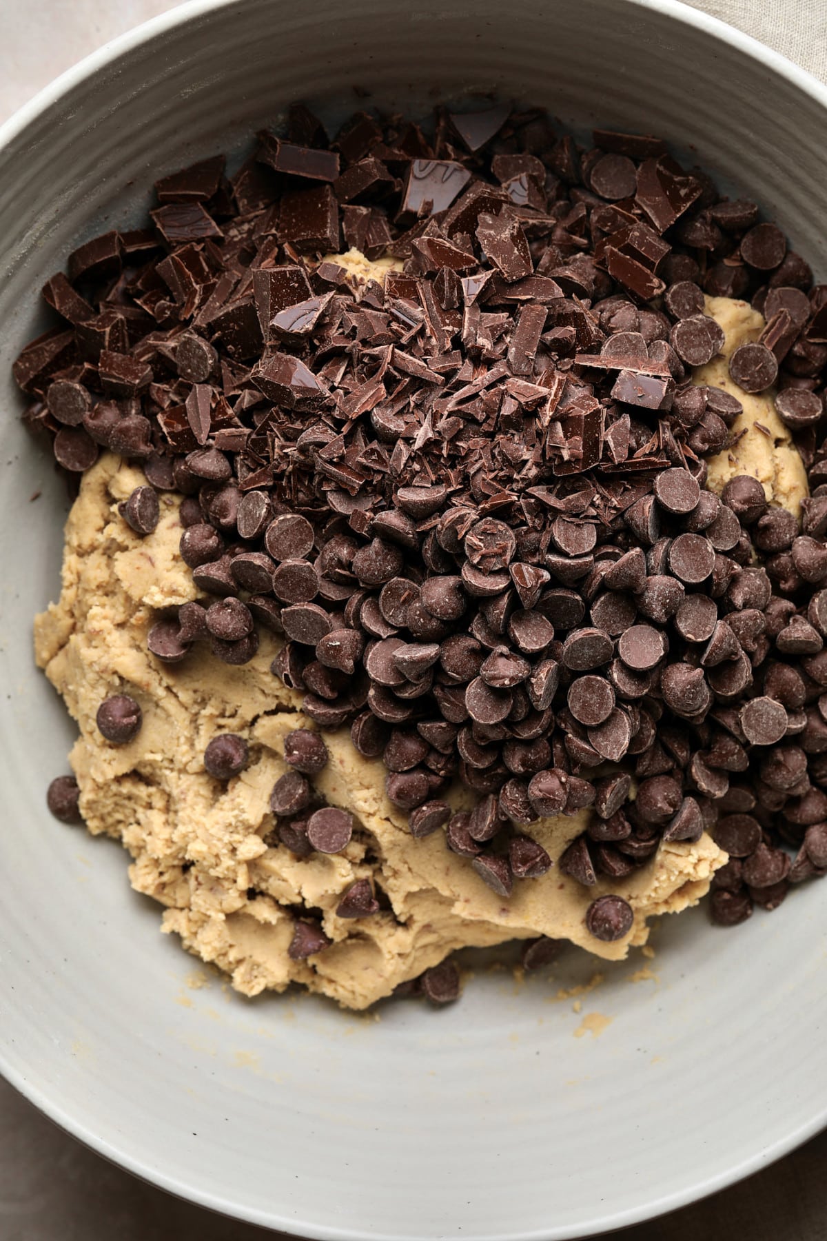 chocolate chips and chunks on top of cookie batter in bowl