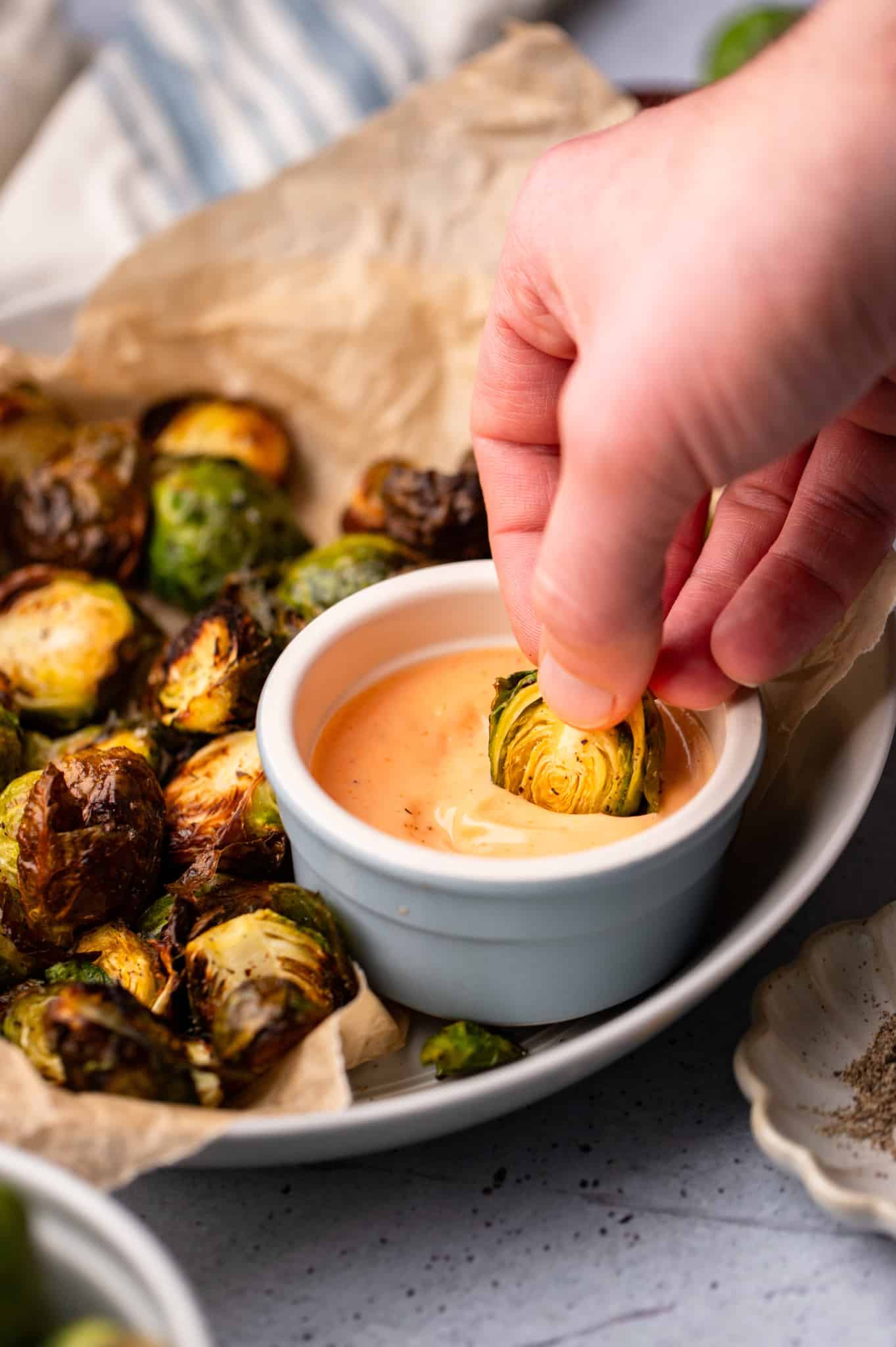 womans hand dipping a cooked brussels sprout in a bowl of chipotle aioli.