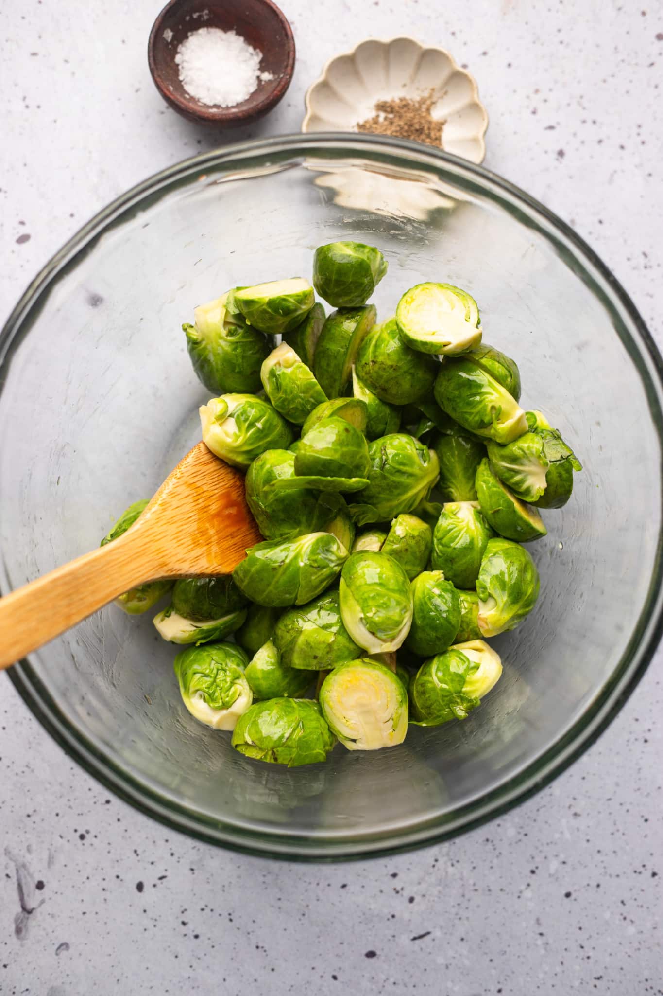 using a wooden spoon to toss brussels sprouts in oil.