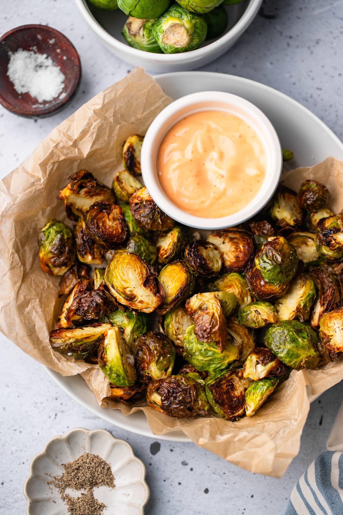 cooked brussels sprouts in a serving bowl with a small bowl of sriracha aioli on the side.