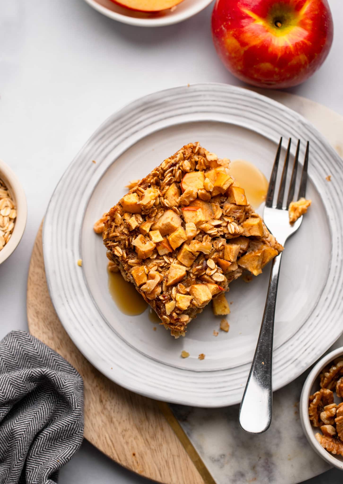 A slice of Apple Baked Oatmeal on a white plate with a fork on the side.