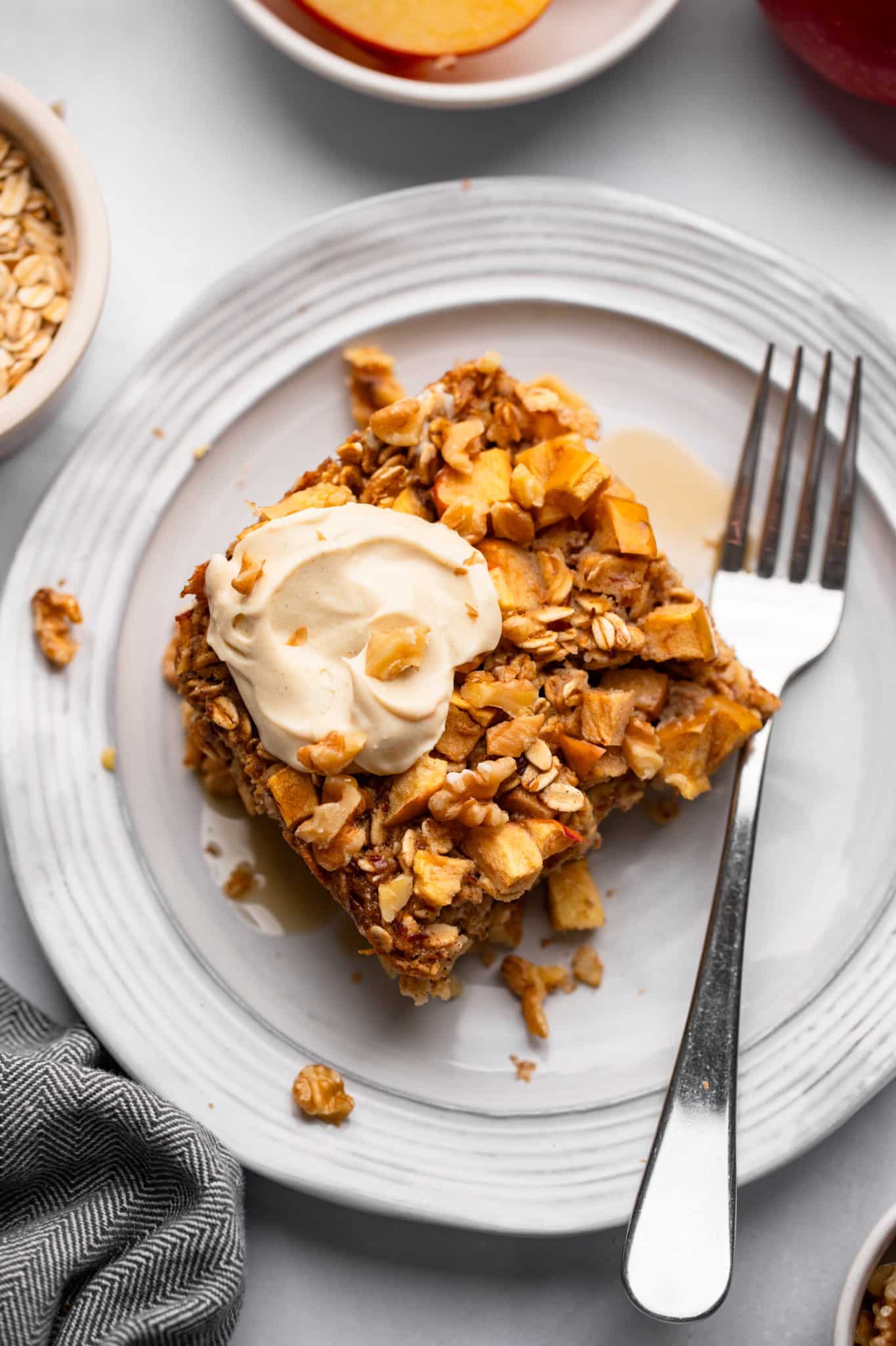 A slice of Apple Baked Oatmeal with a dollop of yogurt on top on a white plate with a fork on the side.