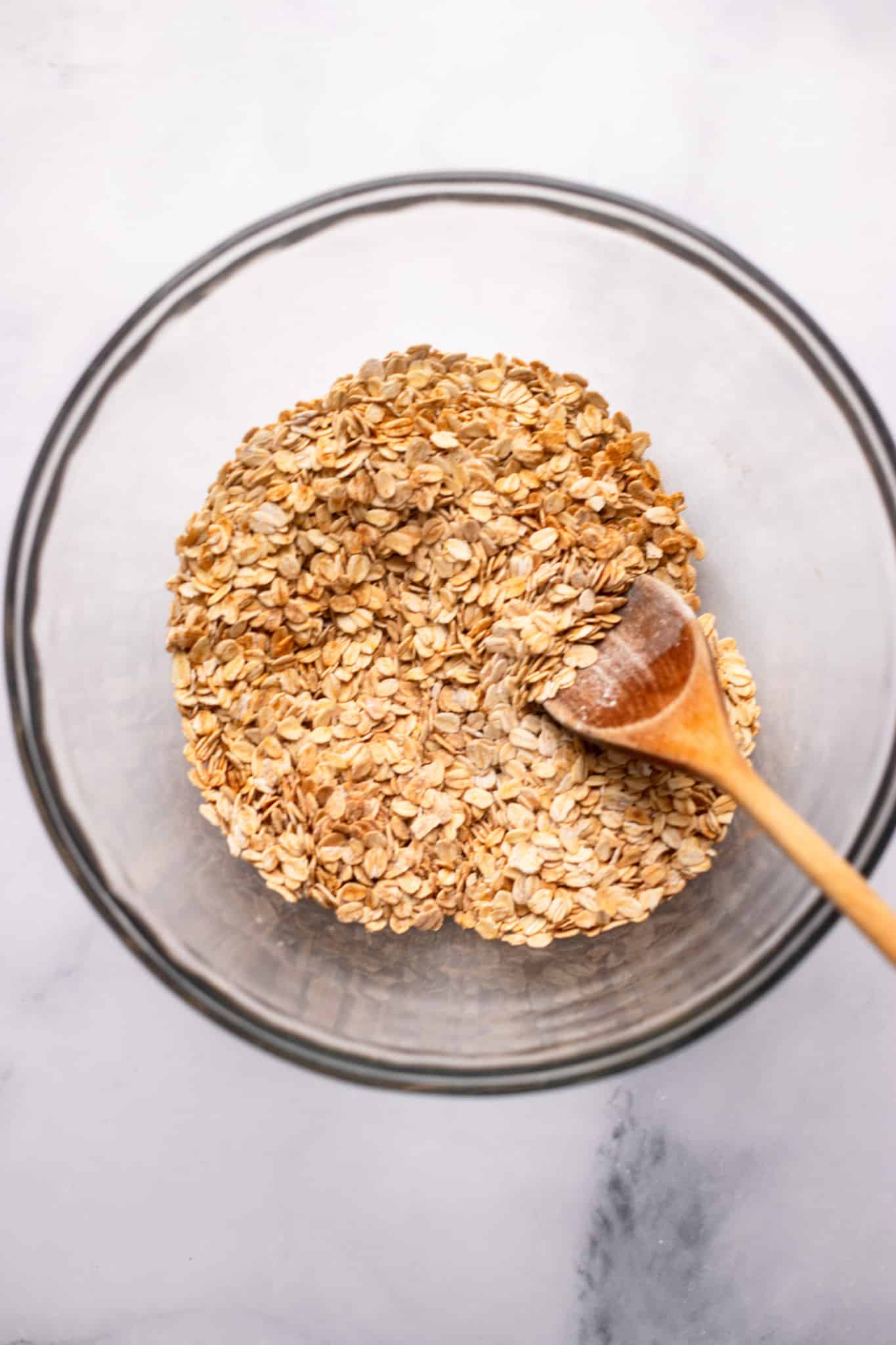 using a wooden spoon to stir oats in a glass bowl.