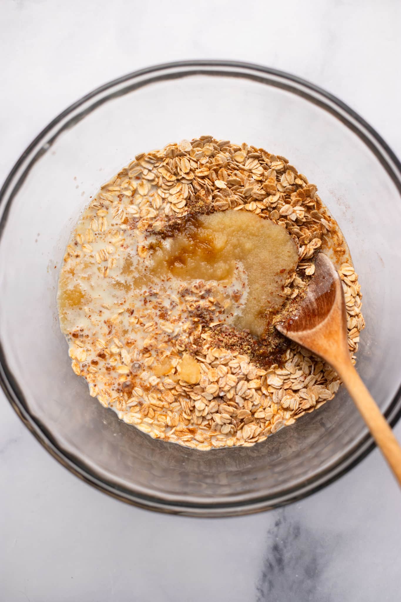 using a wooden spoon to stir the ingredients for apple baked oatmeal in a glass bowl.