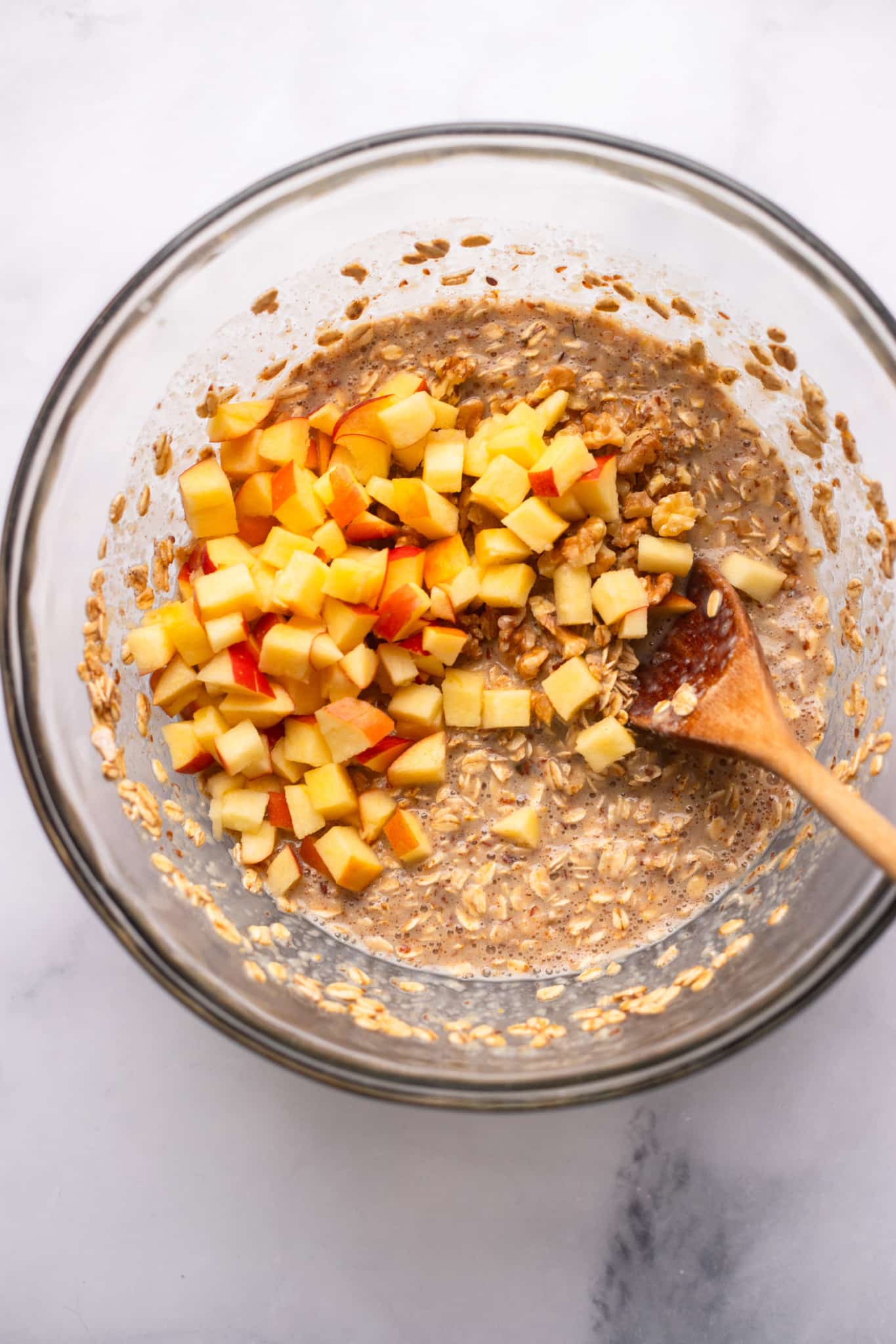 using a wooden spoon to fold chopped apples into an oatmeal mixture.