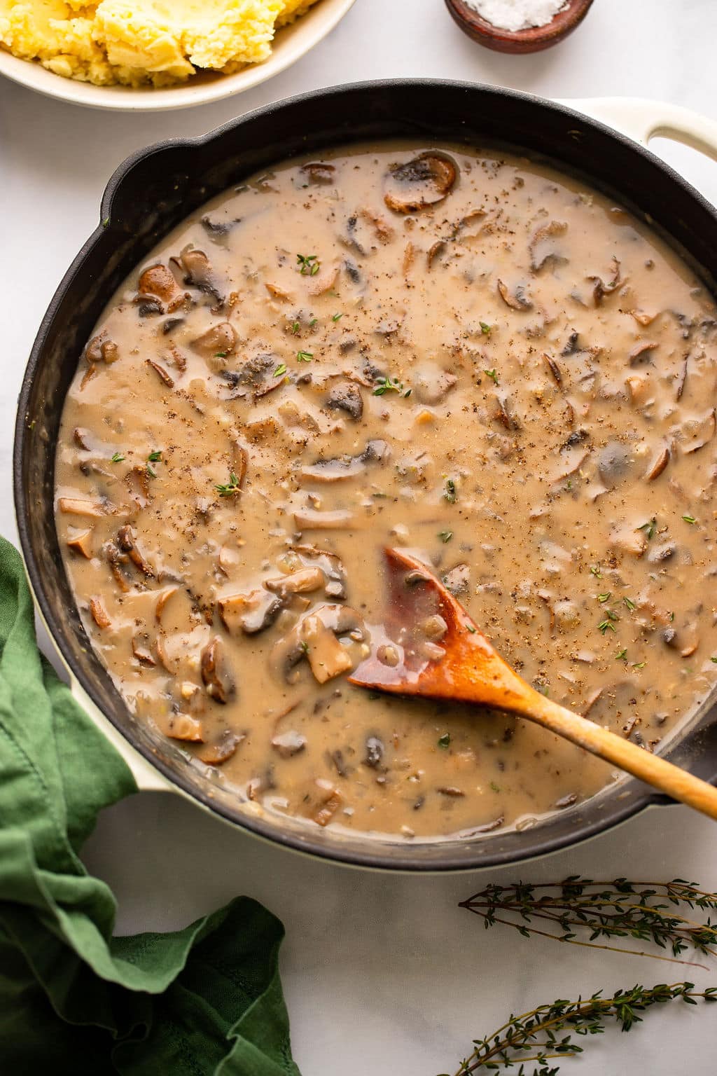 stirring mushroom gravy in a black skillet with a wooden spoon.