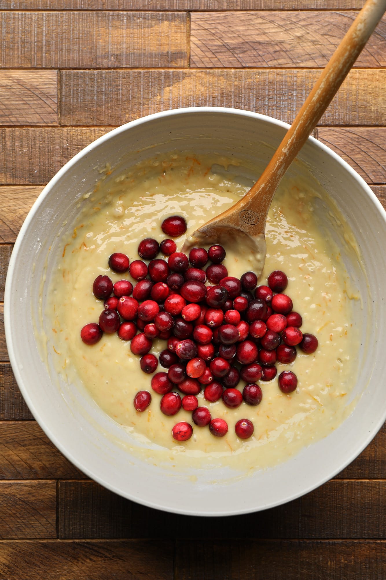 using a wooden spoon to fold whole cranberries into muffin batter.