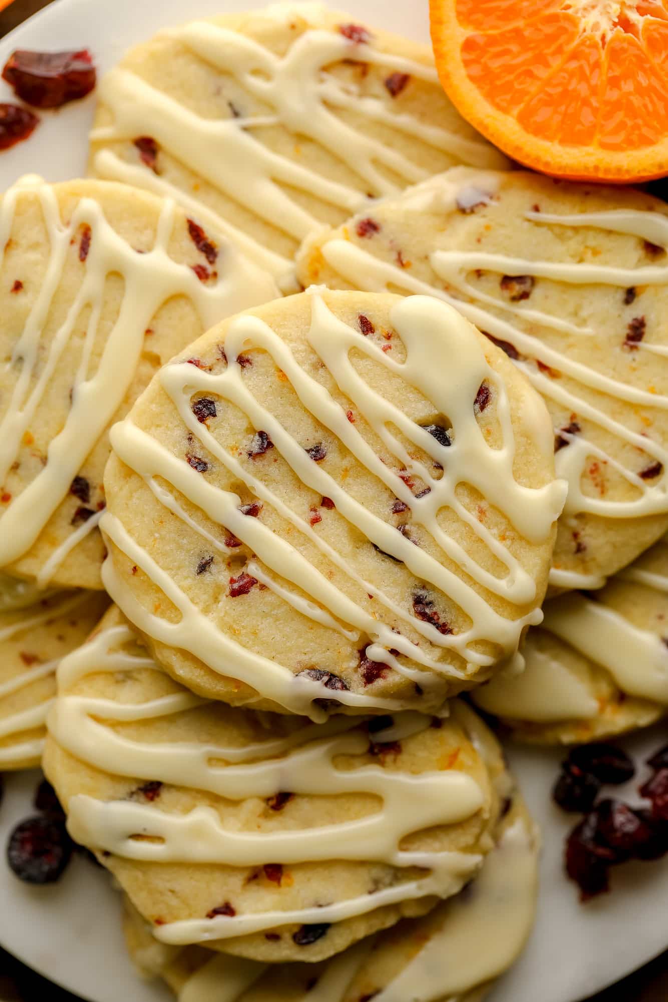 close up on a pile of Orange Cranberry Shortbread Cookies decorated with orange glaze.