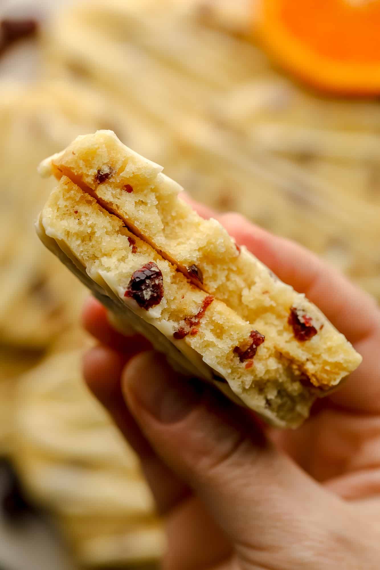 a womans hand holding an Orange Cranberry Shortbread Cookie that's been cut in half.