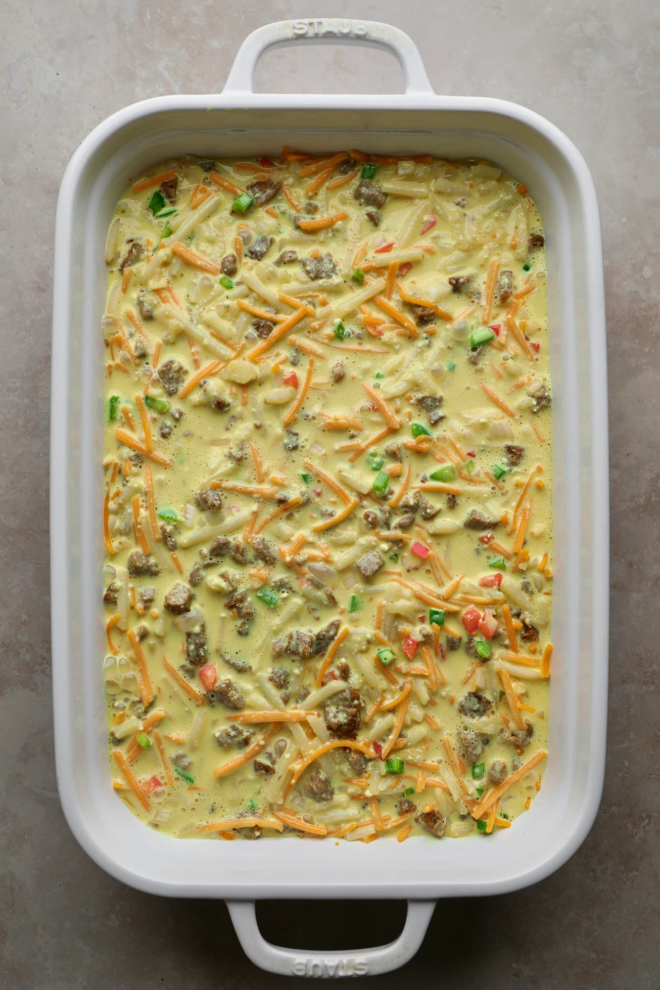 An assembled and unbaked vegan breakfast casserole in a white baking dish.