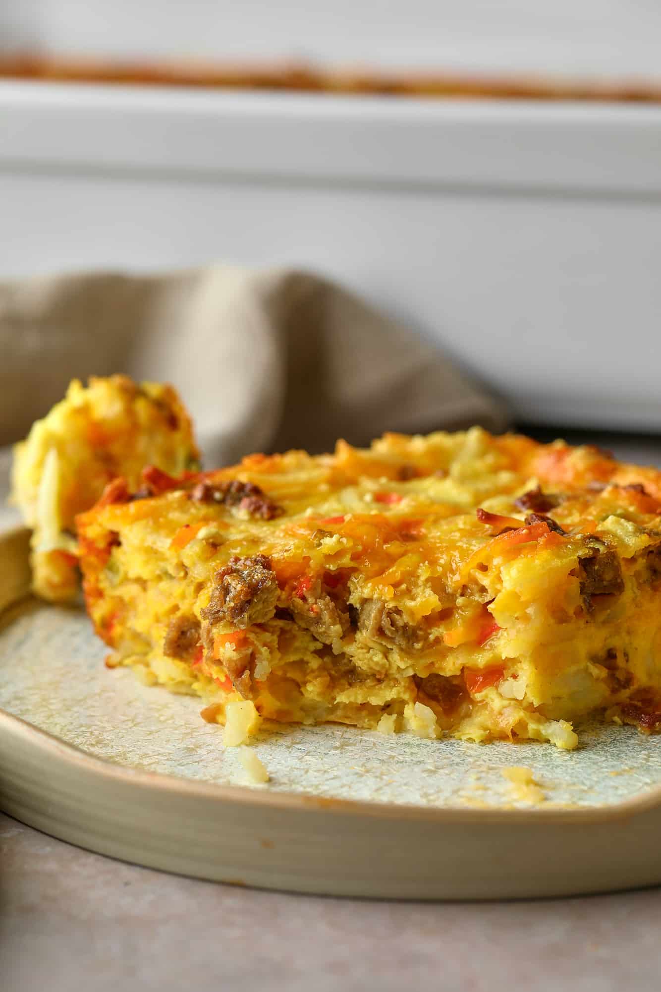 close up on a slice of Vegan Breakfast Casserole on a white plate with a bite removed.