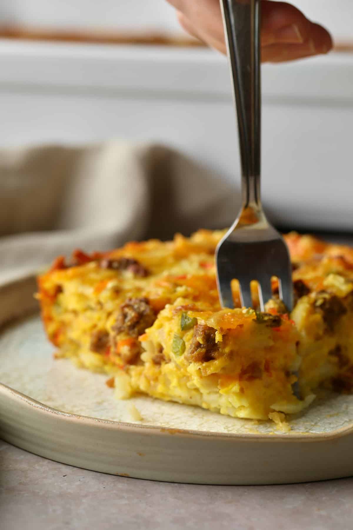 a fork taking a bite out of a slice of vegan breakfast casserole.