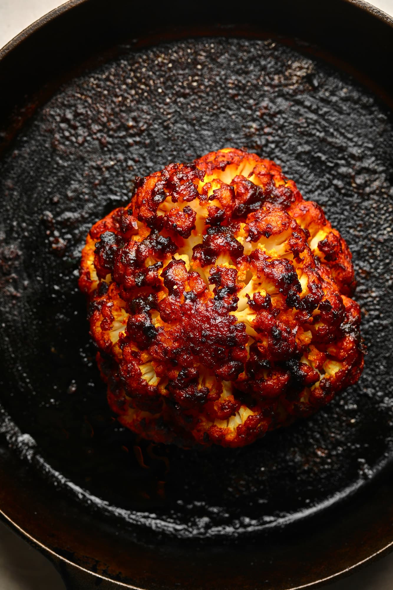 a harissa-glazed roasted cauliflower head in a black skillet.