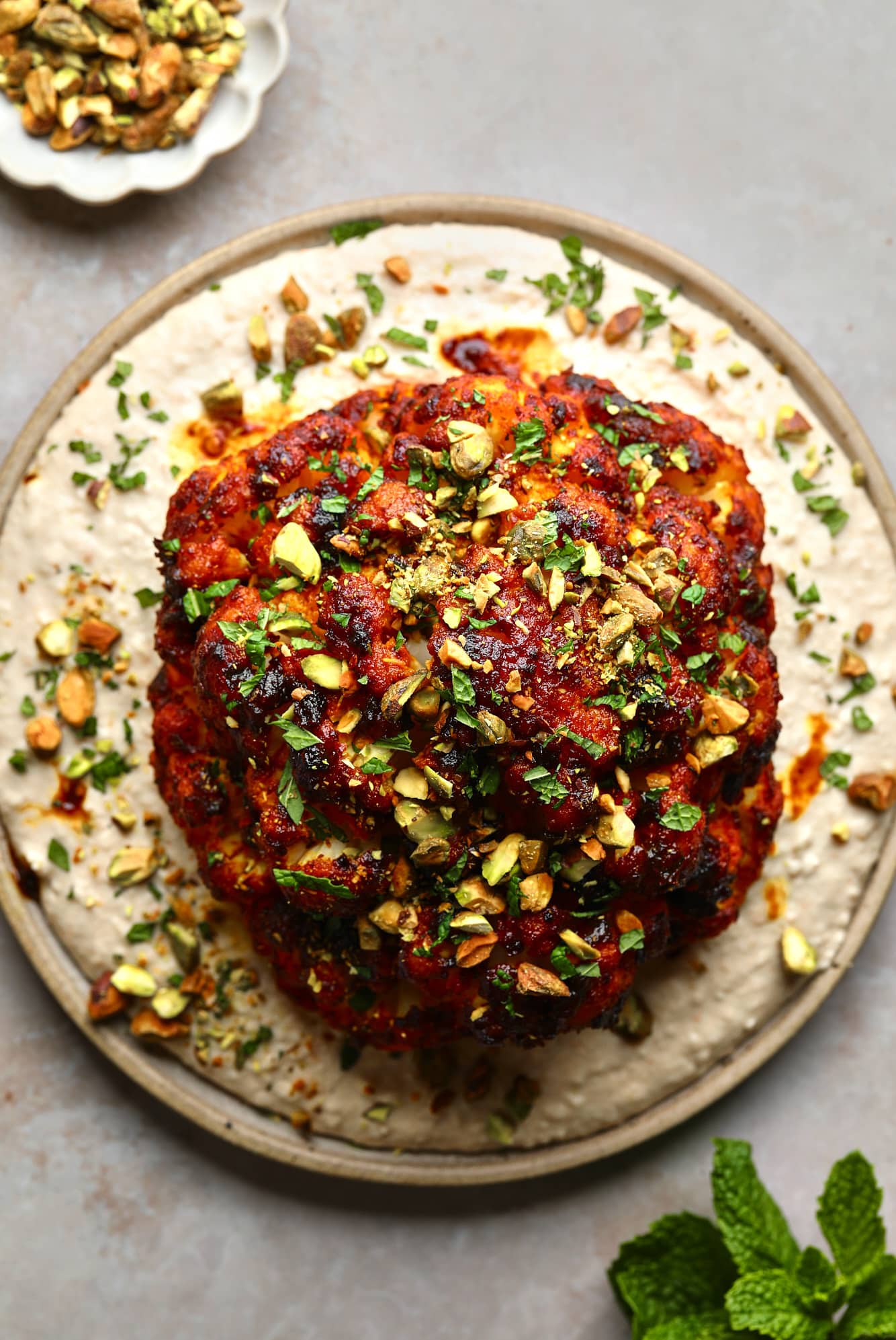 a harissa-glazed roasted cauliflower head on a white bean spread on a plate.