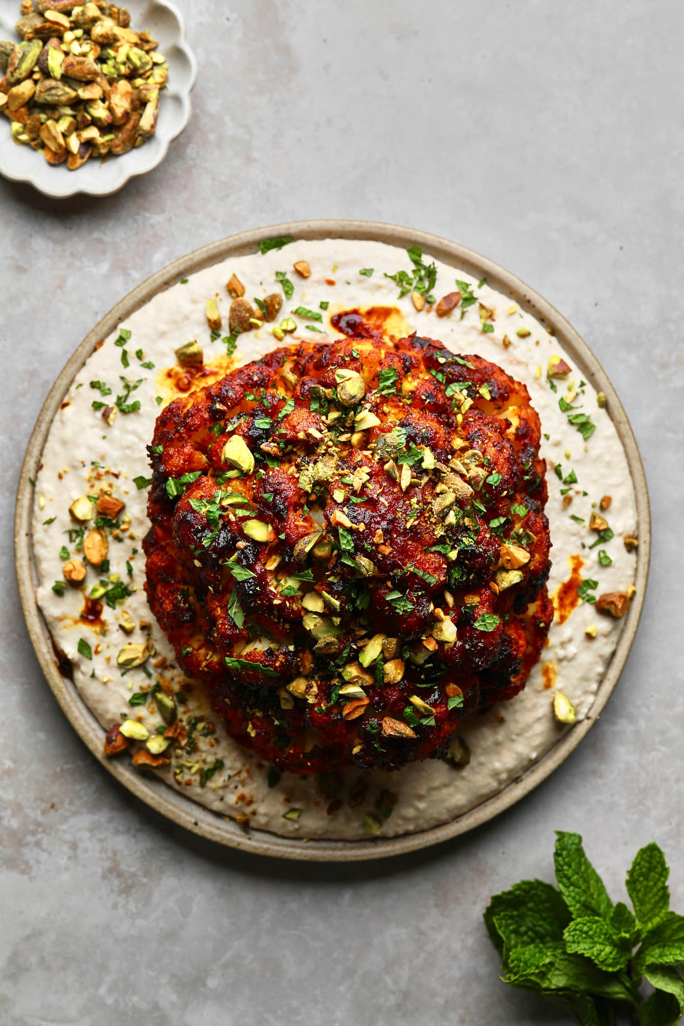 a harissa-glazed roasted cauliflower head on a white bean spread on a plate.