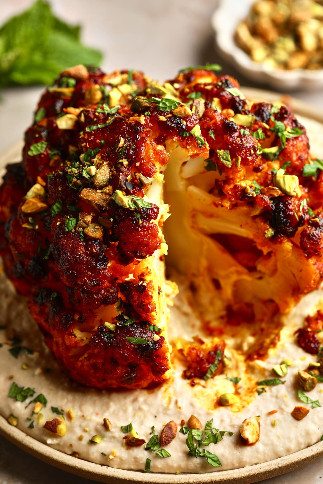 close up on a sliced harissa-glazed roasted cauliflower head on a white bean spread on a plate.