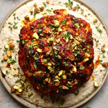 a harissa-glazed roasted cauliflower head on a white bean spread on a plate.