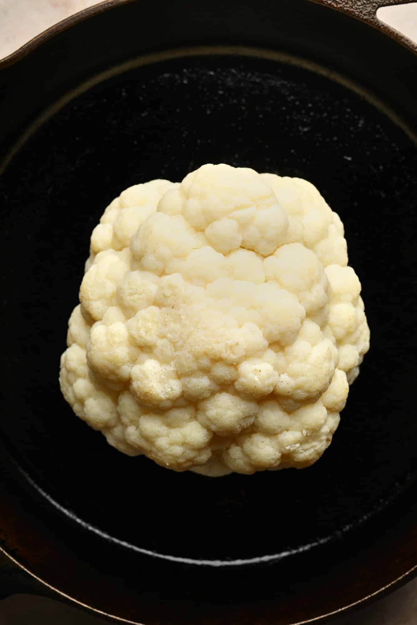 a cauliflower head in a black skillet.