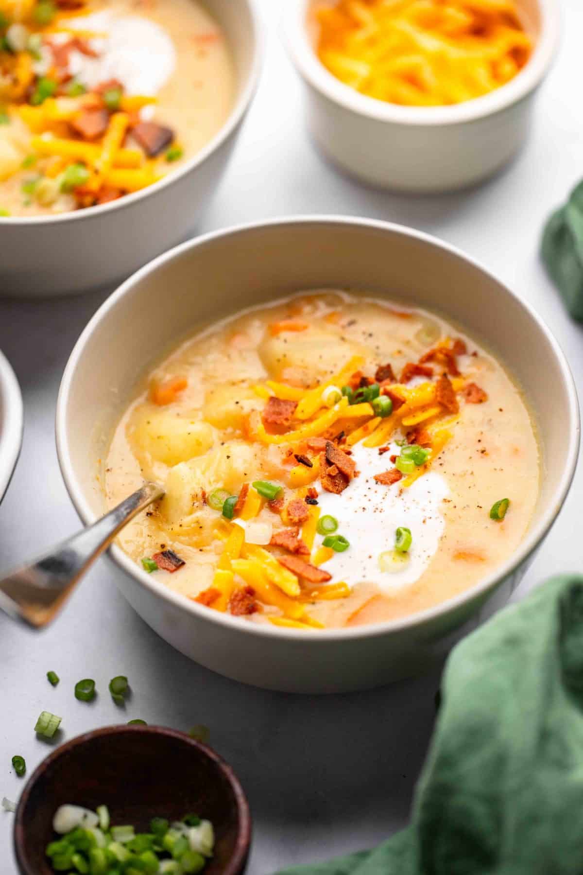 vegan potato soup in cream colored bowl with sour cream and bacon for toppings