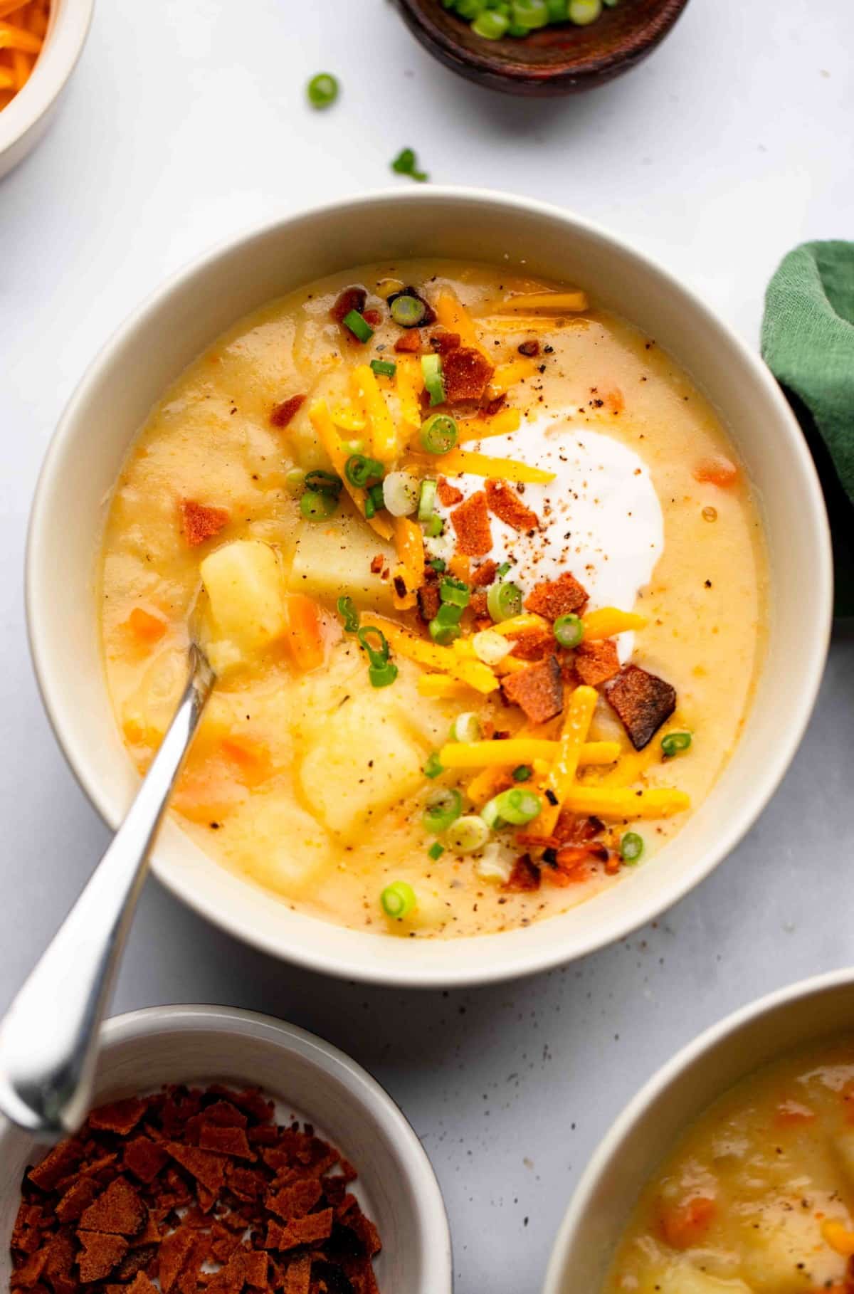 looking down on a bowl of vegan potato soup with toppings on white backdrop