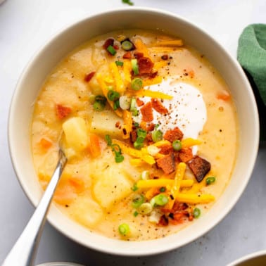 square image of a bowl of potato soup with lots of toppings like bacon, sour cream and cheese