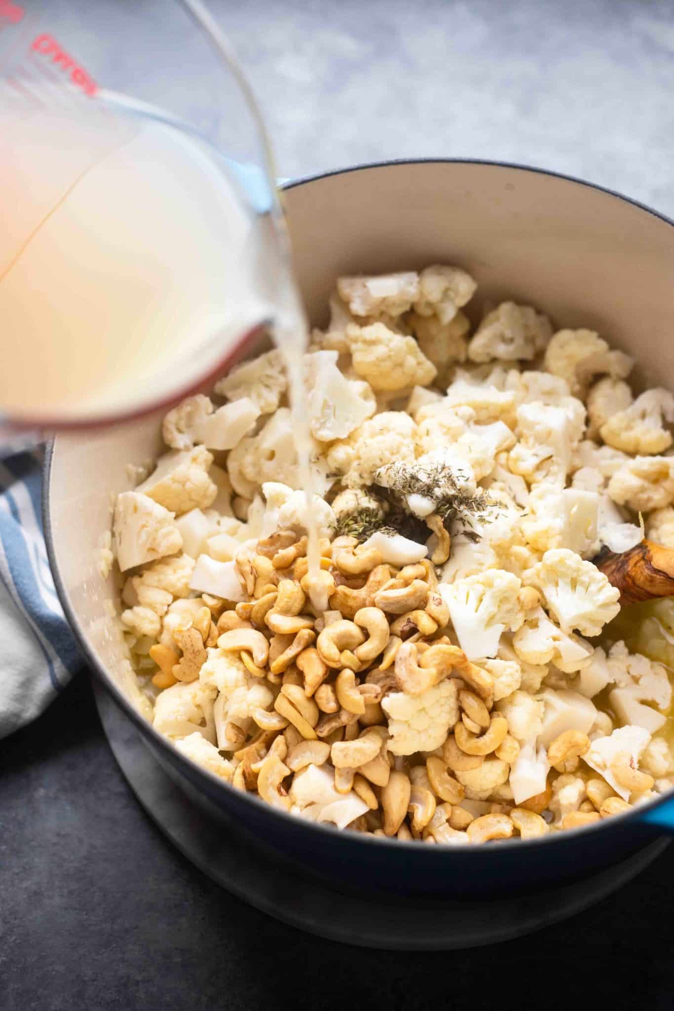 pouring broth over the ingredients for vegan cauliflower soup in a pot.