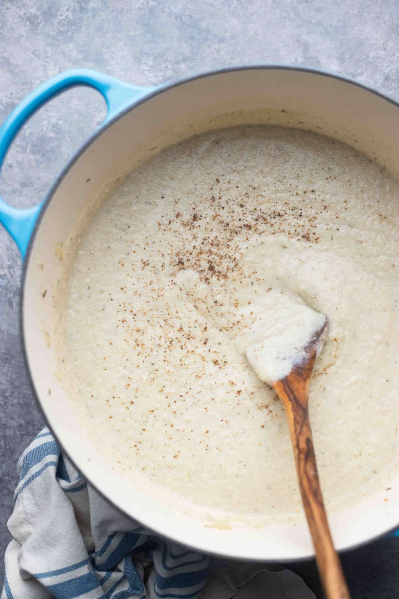 using a wooden spoon to stir vegan cauliflower soup in a large pot.