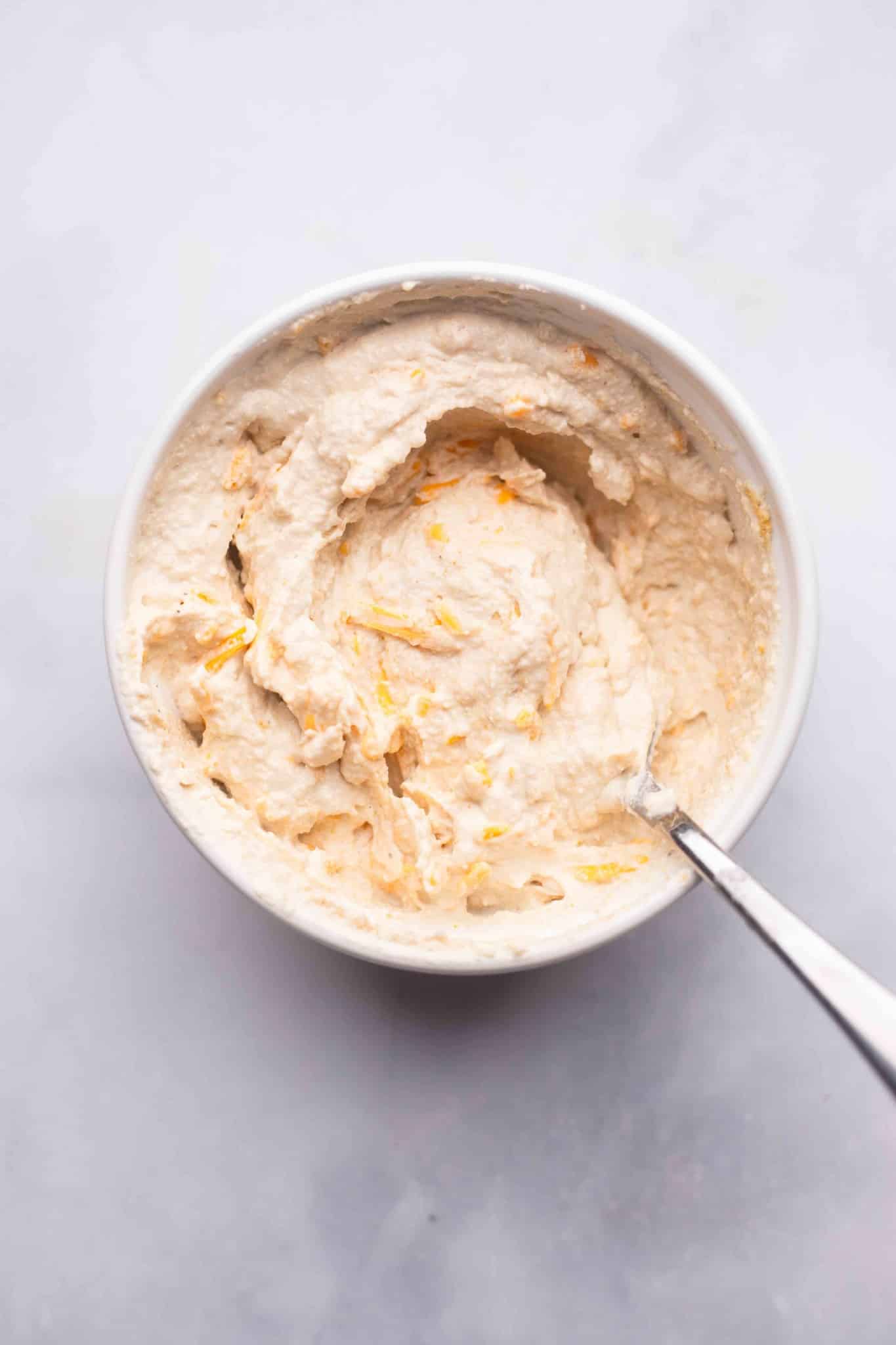 using a spoon to stir a vegan cream cheese mixture in a white bowl.