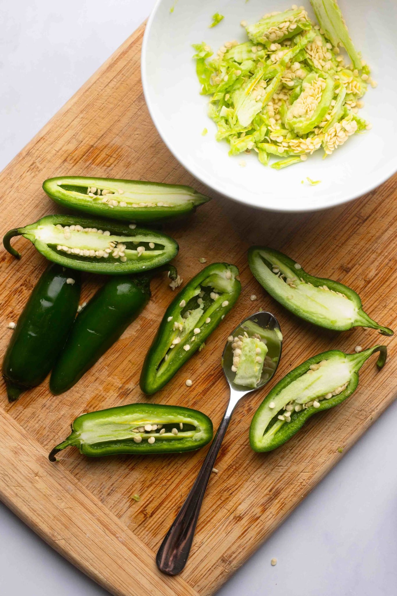 using a spoon to scrape the seeds out of halved jalapeno peppers.