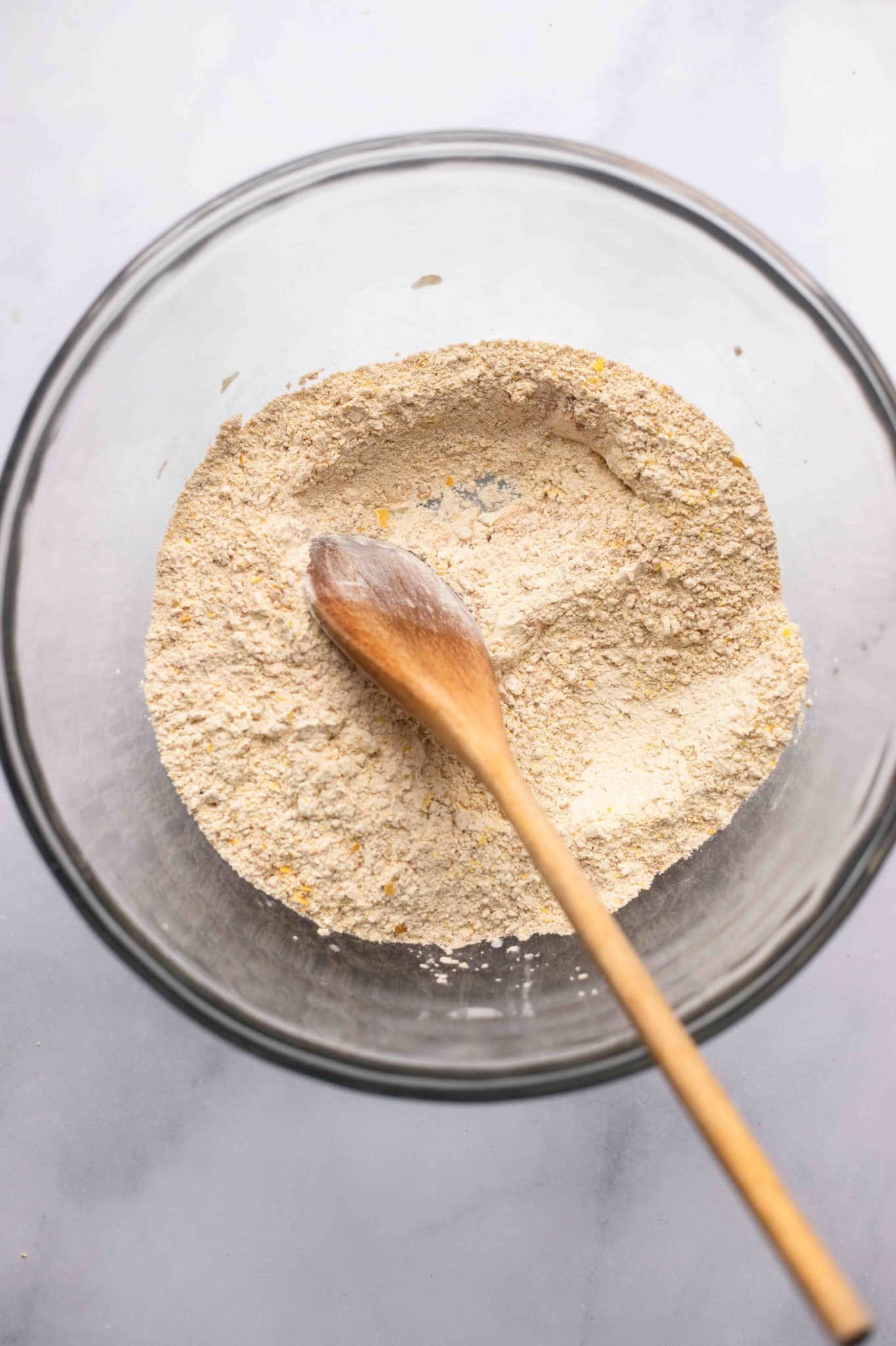 using a wooden spoon to stir a dry flour mixture together in a large bowl.