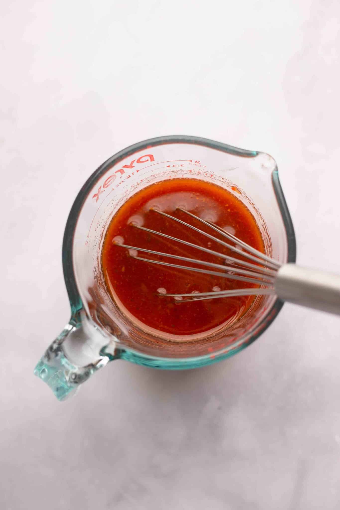 whisking a red liquid in a glass measuring cup.