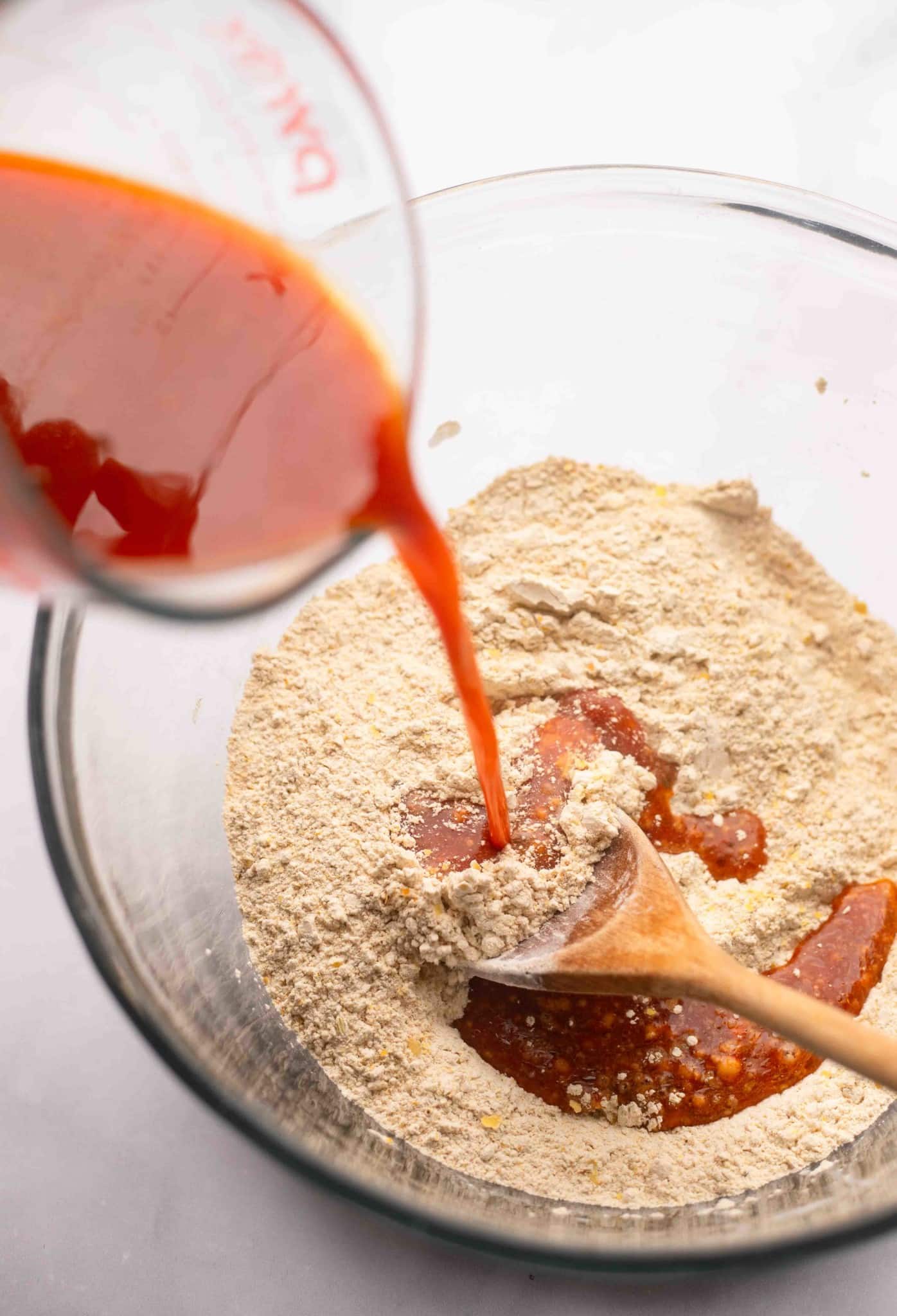 pouring red liquid into a dry flour mixture in a large bowl.