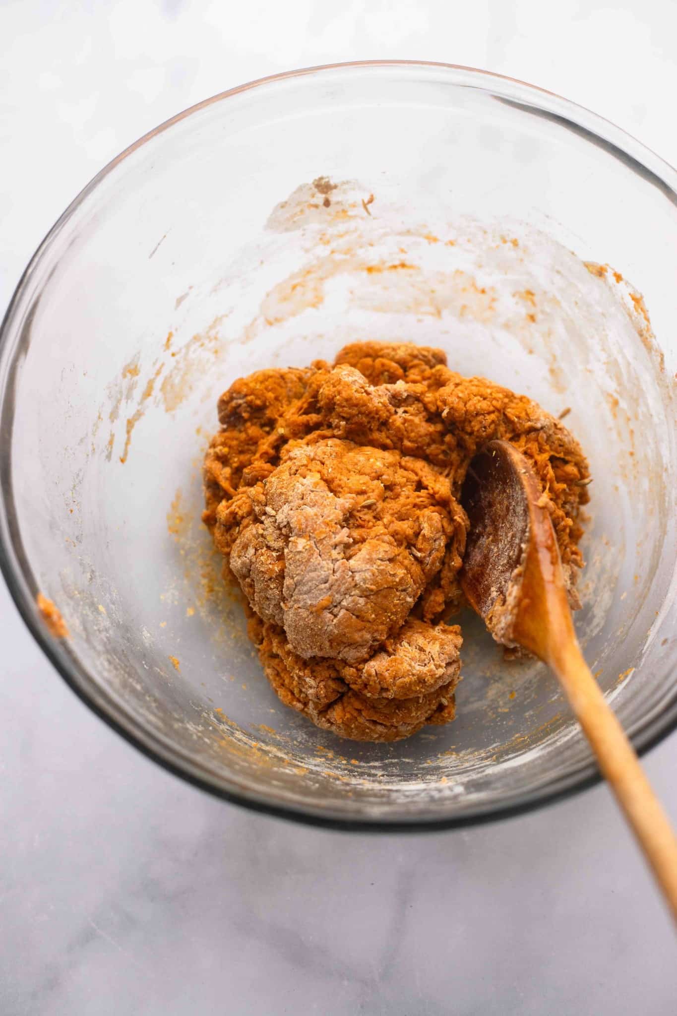 using a wooden spoon to stir the vegan pepperoni ingredients into a dough in a glass bowl.