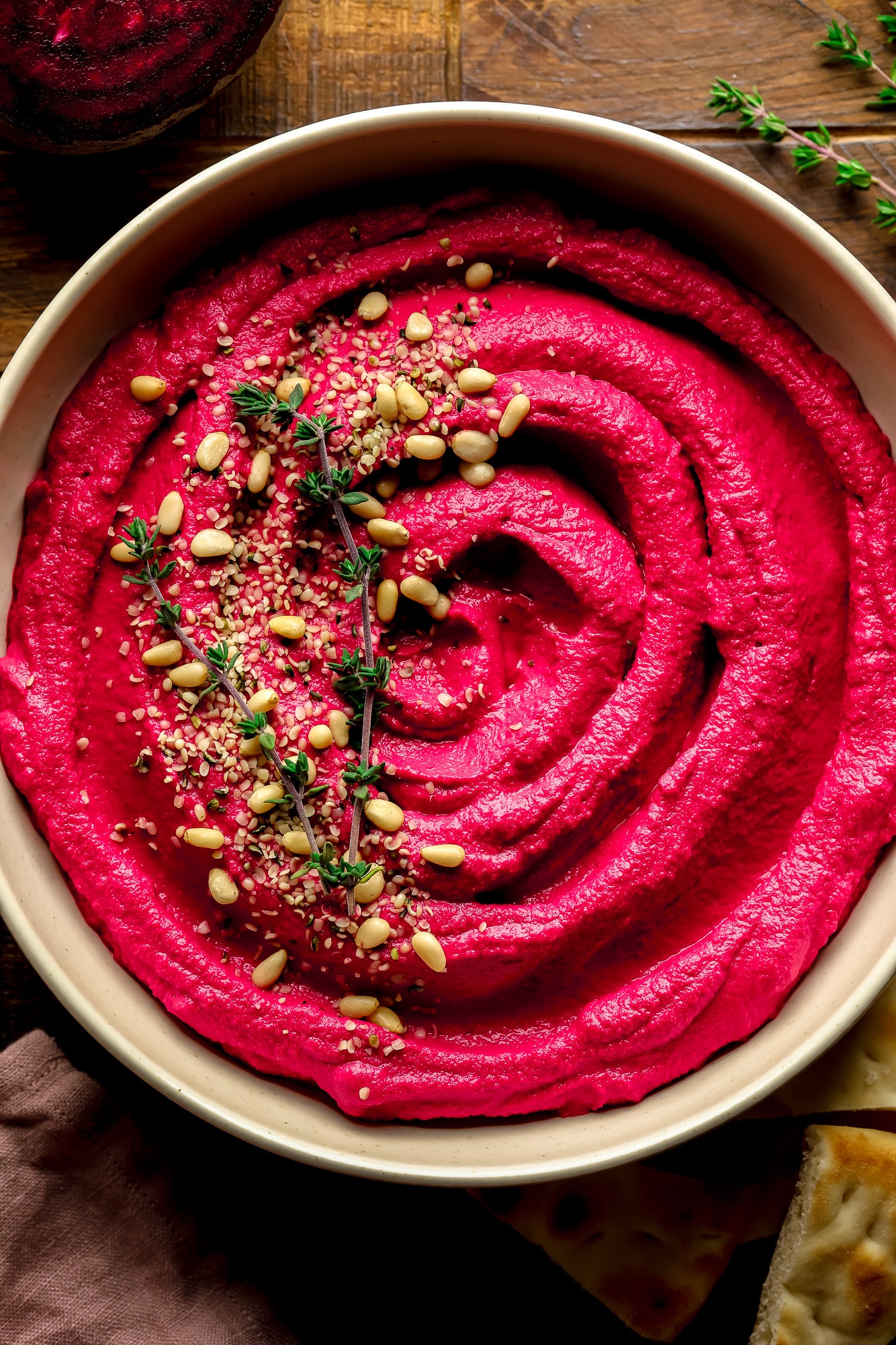 a bowl of pink beet hummus with pine nuts and thyme on top.